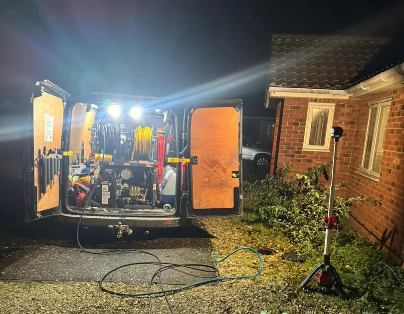 Emergency drainage King's Lynn night-time callout showing a drainage van with rear doors open, specialist equipment illuminated and hoses running across a gravel driveway beside a residential property.