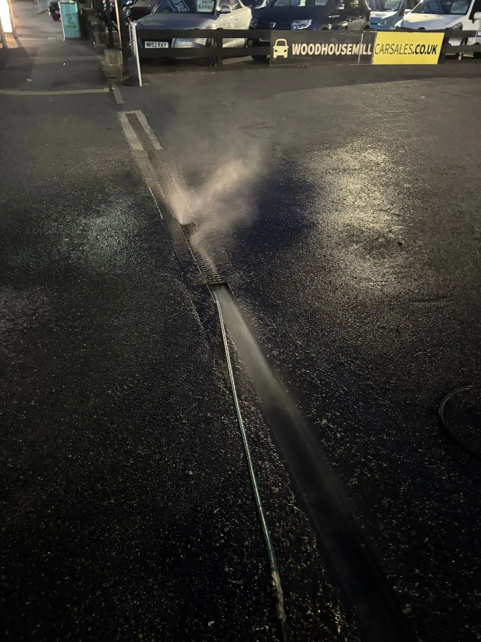 High-pressure water jetting cleaning a channel drain in King’s Lynn at night.