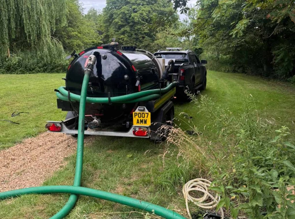 Septic tank emptying equipment and suction hoses set up beside a black tanker trailer at a rural Norfolk property.